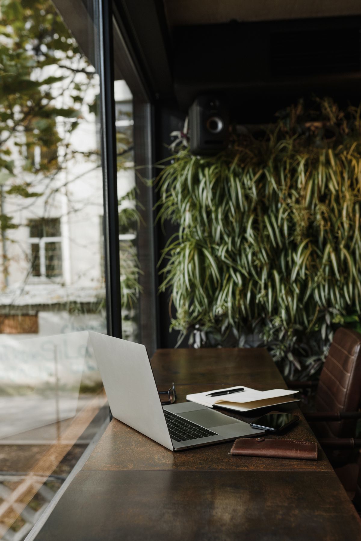 A calm garden office interior — laptop on a timber desk, full-height glazing looking out to greenery